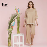 Woman in beige outfit standing next to a white stool with floral arrangements on a pink background